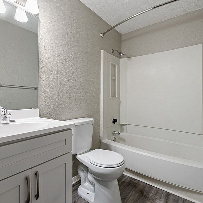 Elegant modern bathroom featuring sleek white fixtures, a spacious bathtub, and stylish cabinetry on a chic wood floor.