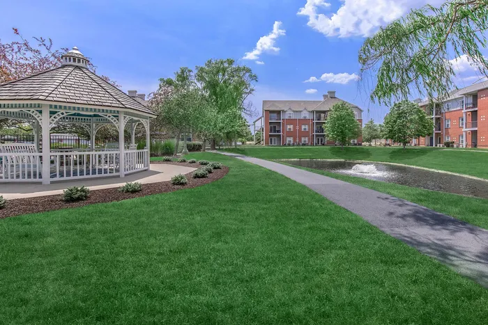 Serene apartment community featuring a charming gazebo, lush green lawns, and a sparkling pond with a fountain.