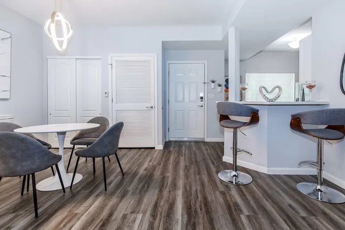 Modern apartment entrance with chic dining area, elegant round table, and stylish bar seating under a contemporary light fixture.