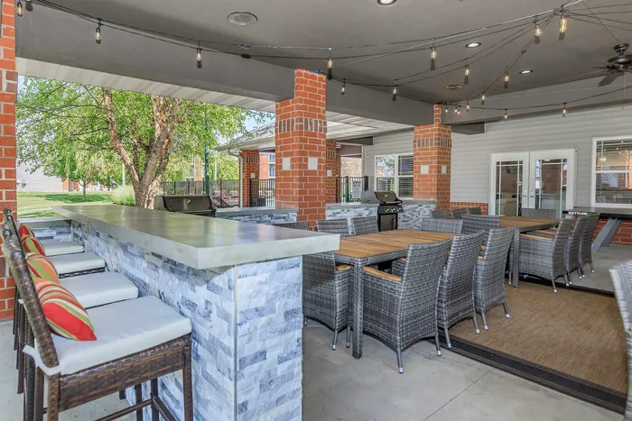Chic outdoor patio space featuring cozy wicker seating, a stylish stone bar with modern stools, and ambient string lighting.