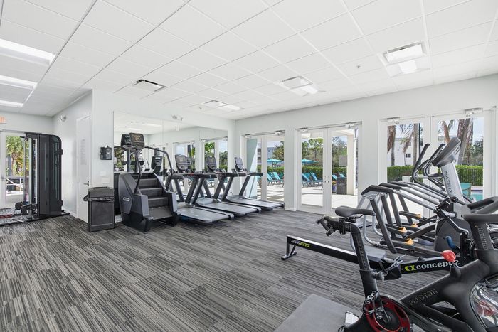 Bright, modern fitness center equipped with treadmills, exercise machines, and large windows overlooking a swimming pool area.