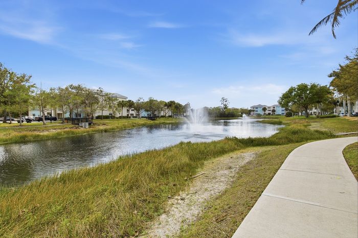 Serene apartment setting with tranquil pond view, fountains, and lush greenery along a scenic walking path.