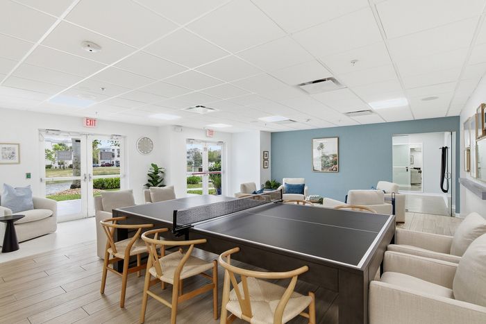 Bright and inviting recreation room with a modern ping pong table, comfortable seating, and large windows offering serene garden views.