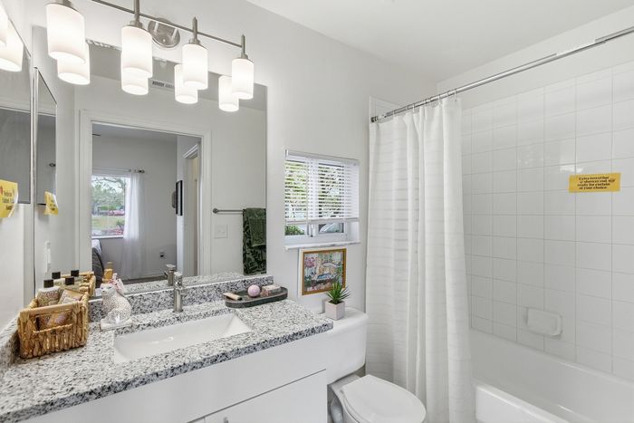 Bright and modern bathroom featuring a sleek granite countertop, elegant lighting fixtures, and a stylish tiled shower with a curtain.