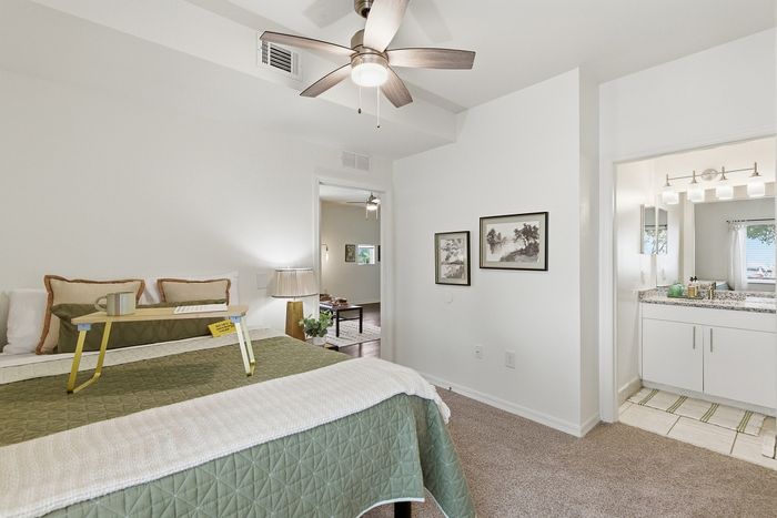 Cozy bedroom with elegant decor featuring a ceiling fan, plush bed with stylish linens, and a modern en-suite bathroom with granite countertops.