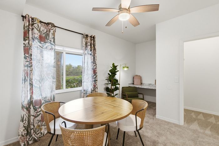 Bright dining room with a round wooden table, stylish chairs, floral curtains, and a modern ceiling fan.
