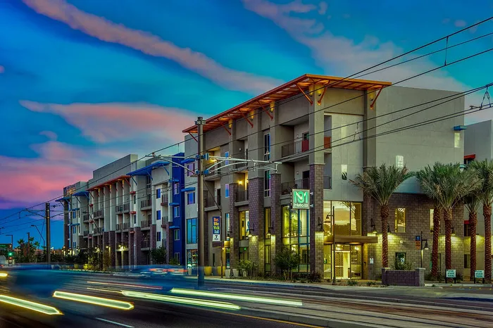 Vibrant street view of modern apartment building at twilight, featuring colorful sky and dynamic street lights.