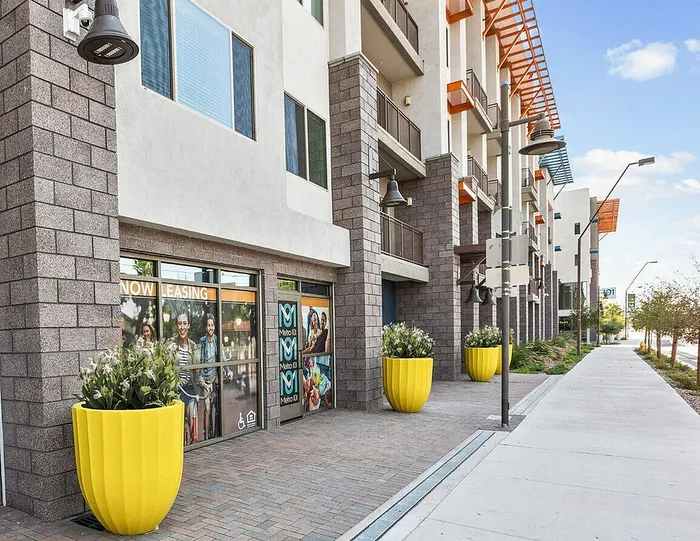 Modern apartment complex with stylish architecture, vibrant yellow planters, and a prominent leasing sign, showcasing a welcoming urban living environment.