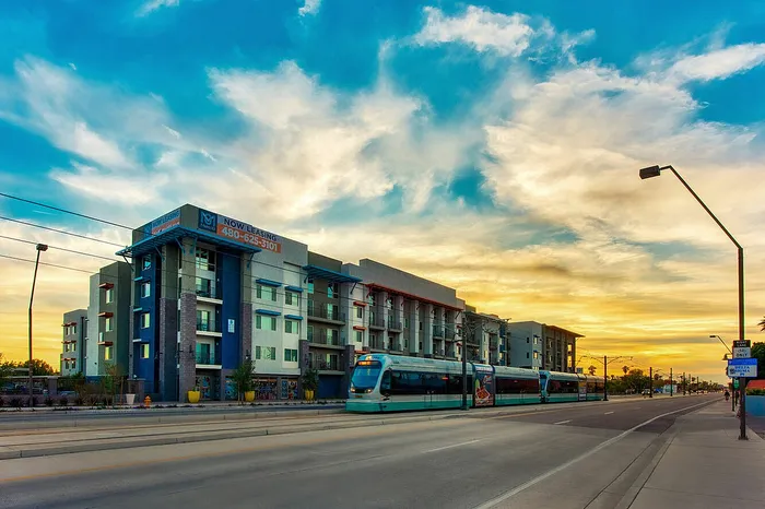 Modern apartment building with urban transit access framed by a vibrant sunset sky.