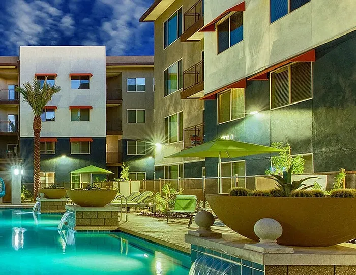 Luxurious apartment complex with a glistening outdoor pool, modern architecture, and inviting lounge areas under evening skies.