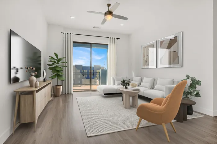 Modern living room with a chic white sofa, large flat-screen TV, cozy orange armchair, and a large window offering bright natural light.