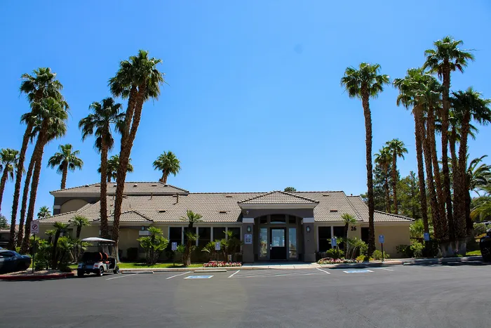 Inviting apartment complex entrance surrounded by tall palm trees and sunny skies, offering a serene and welcoming atmosphere.