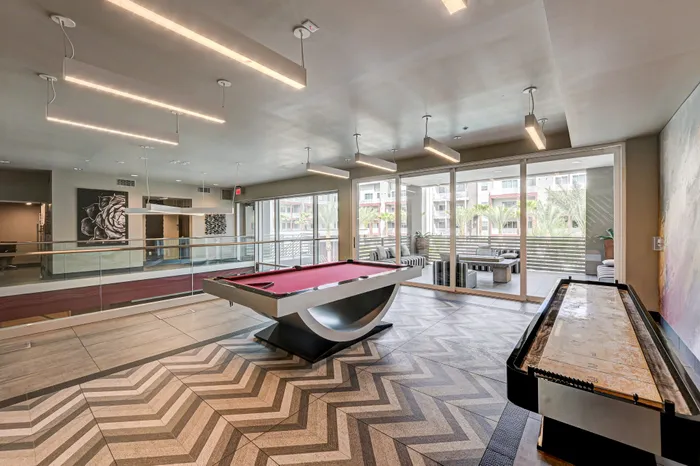 Modern recreational room with a stylish pool table, sleek lighting, and a chevron-patterned floor, offering a luxurious indoor-outdoor ambiance.