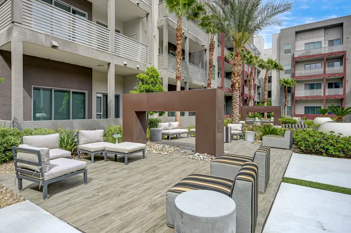 Modern apartment complex courtyard featuring stylish outdoor seating, lush greenery, and palm trees under a clear blue sky.
