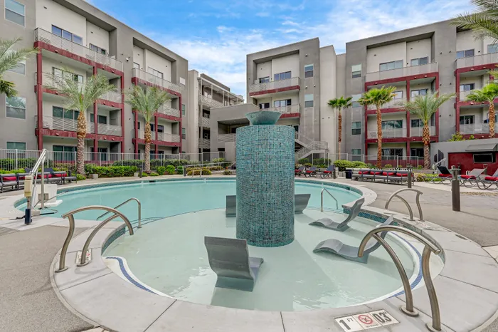 Modern apartment complex with luxurious poolside lounge area, stylish pool chairs, and palm tree-lined surroundings.