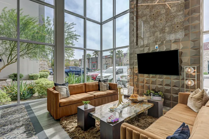 Elegant apartment lounge with large floor-to-ceiling windows, luxurious brown sofas, and a sleek marble coffee table, offering a bright and inviting space.