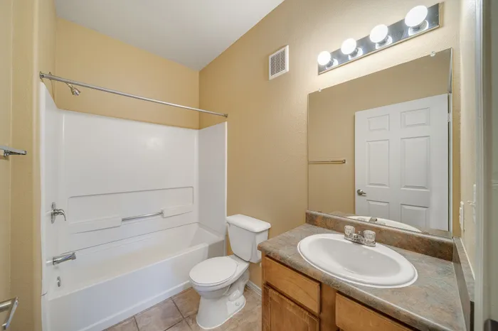Bright and inviting bathroom with modern lighting, spacious mirror, and a pristine bathtub for a relaxing experience.