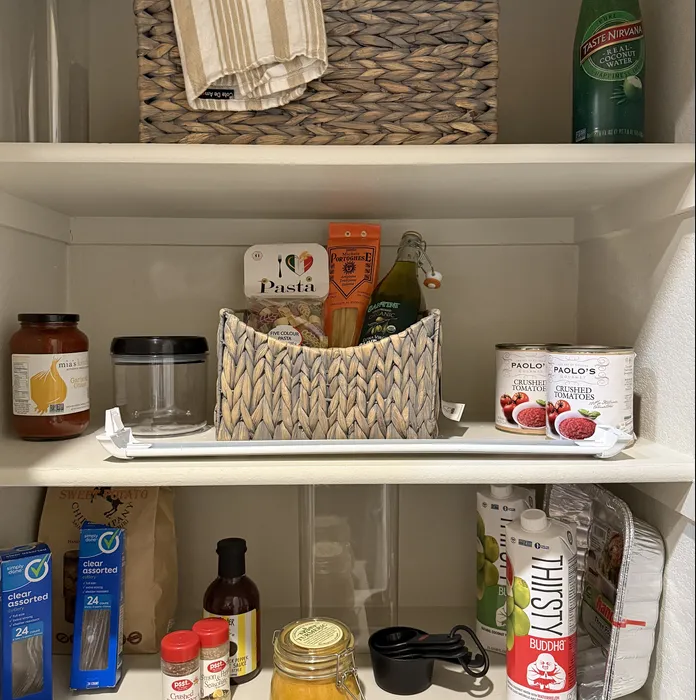 Organized kitchen pantry with diverse selection of gourmet items, including olive oil, herbal drinks, and basket storage enhancing modern apartment convenience.