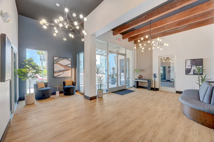 Modern and inviting apartment lobby with stylish lighting fixtures, wooden beams, elegant seating area, and large windows offering abundant natural light.