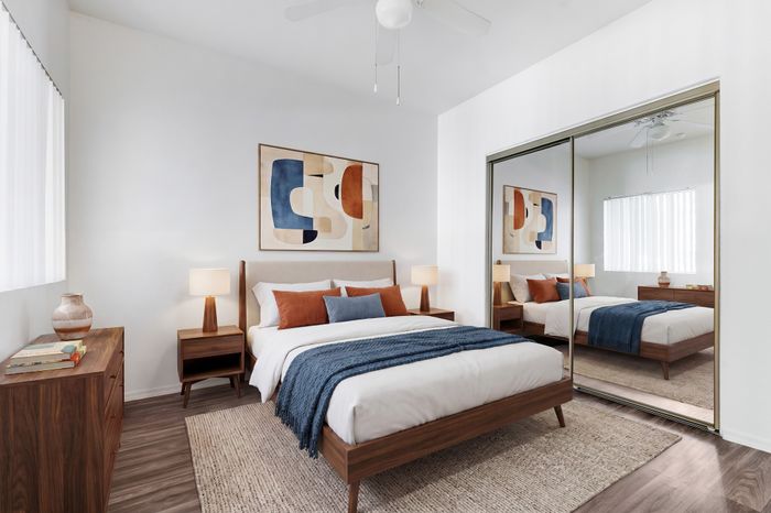 Inviting bedroom featuring a modern wooden bed, cozy blue and terracotta accents, and a large mirror closet.