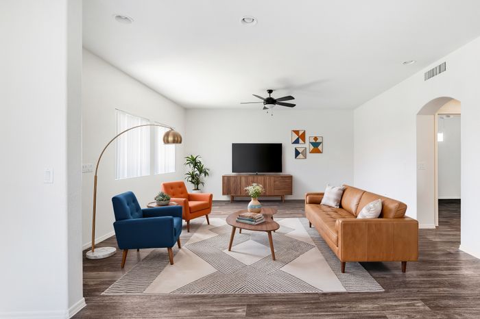 Modern living room with stylish furniture, featuring a leather sofa, colorful armchairs, artistic decor, and a sleek entertainment area.
