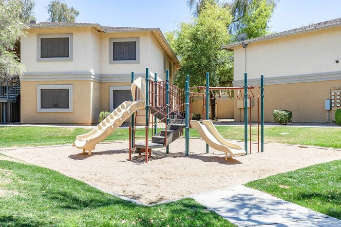 Charming residential community with a modern playground set against a backdrop of well-maintained greenery and contemporary apartment buildings.