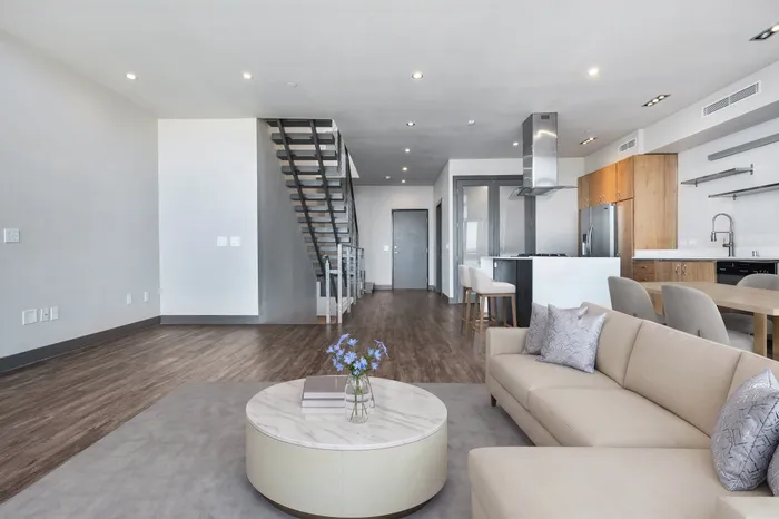 Modern open-concept living space with sleek hardwood floors, elegant staircase, cozy seating area, and stylish kitchen.
