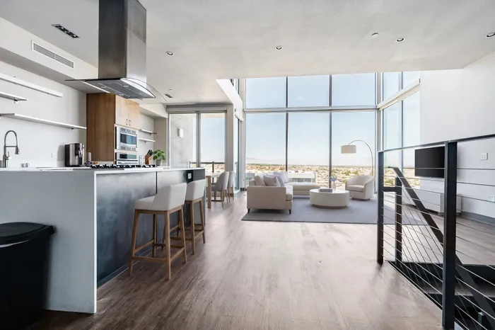 Luxurious open-concept apartment with modern kitchen, sleek white cabinetry, large floor-to-ceiling windows, and a breathtaking city view.