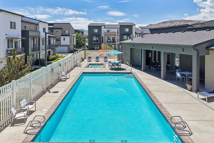 Inviting apartment complex with a sparkling outdoor pool, adjacent spa, and stylish lounge area, set against a backdrop of modern townhomes and scenic mountain views.