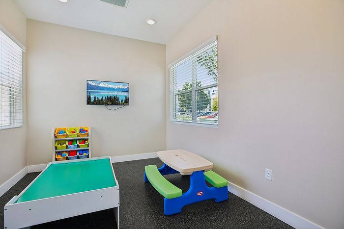 Bright children's playroom featuring a colorful activity table, toy storage, and scenic wall-mounted TV, perfect for fun and learning.