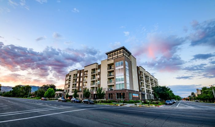 Modern apartment building on a quiet street, with a stunning sunset sky and mountain views, offering luxurious living in a serene environment.