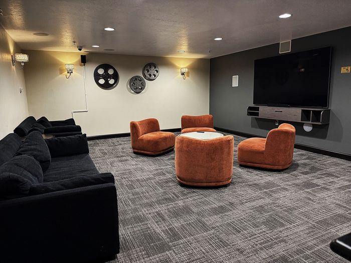 Chic media room with plush black sofas, vibrant orange chairs, and a large wall-mounted TV, perfect for entertainment.