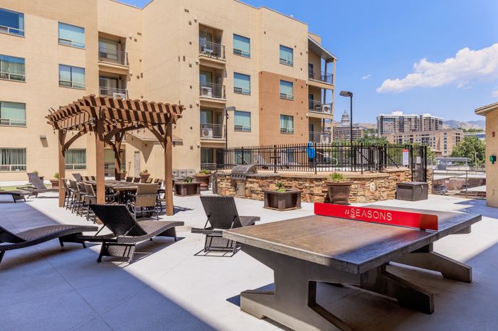 Chic apartment courtyard featuring stylish lounge chairs, a pergola with outdoor seating, and urban skyline views.
