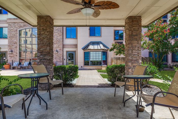 Charming courtyard view with stylish outdoor seating under a covered patio, surrounded by lush greenery and modern architectural details.