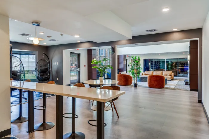Modern community lounge featuring a sleek bar area, cozy seating with plush chairs, and vibrant greenery for a welcoming atmosphere.