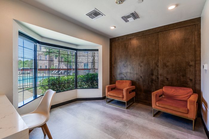 Bright and inviting room featuring modern orange chairs, a sleek white desk, and large windows with scenic outdoor views.