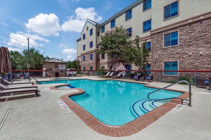 Inviting outdoor pool area with lounge chairs and surrounded by a modern apartment building under a clear blue sky.