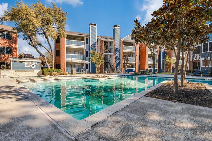 Resort-style outdoor swimming pool surrounded by modern three-story apartment buildings and trees at Preferred Place Apartments in Houston&rsquo;s Energy Corridor.
