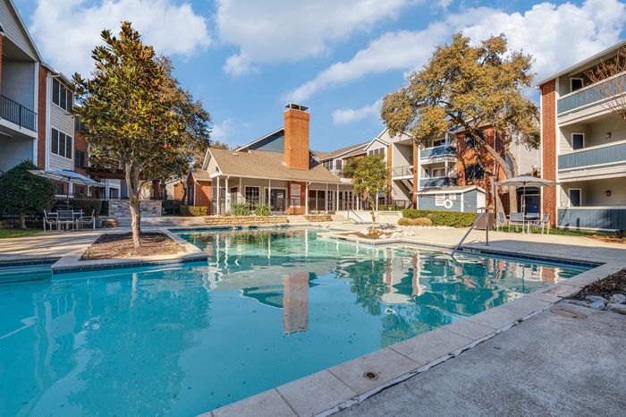 Outdoor swimming pool surrounded by modern apartment buildings and trees at Preferred Place Apartments in Houston TX.
