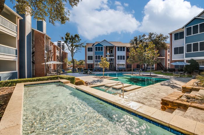Outdoor swimming pool and shallow water feature surrounded by apartment buildings and trees at Preferred Place Apartments in Houston TX.