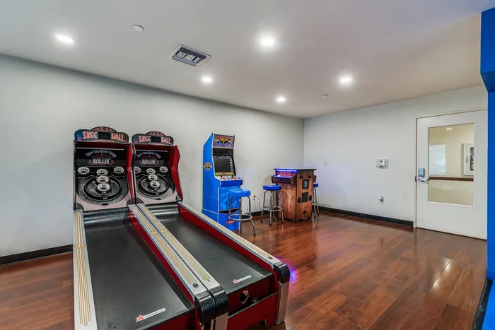 An arcade style game room featuring skee ball lanes, a retro arcade machine, and a small seating area with bar stools.