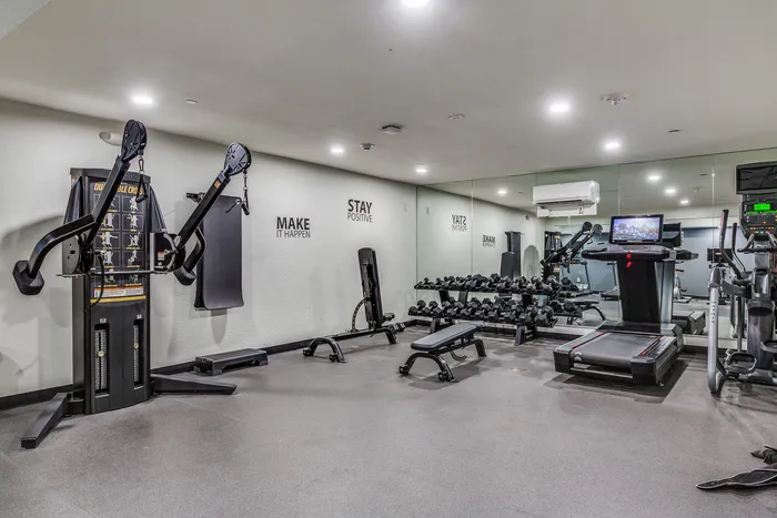 Indoor gym with cardio machines, weight benches, dumbbells, and mirrored walls.