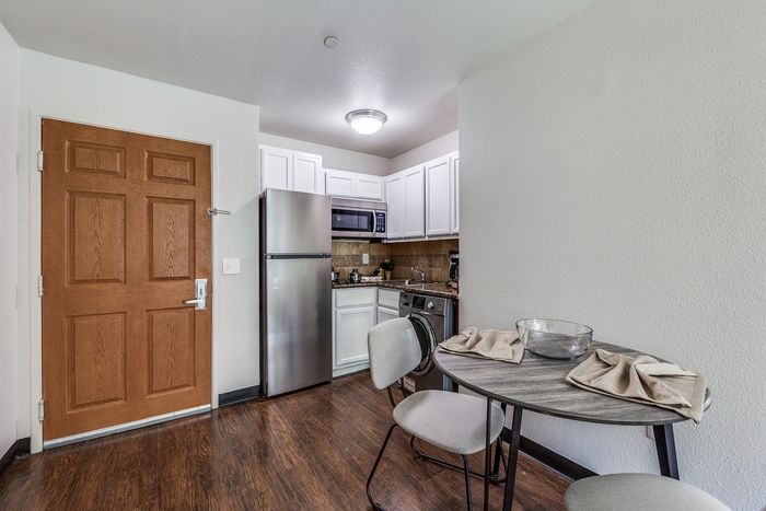 A compact kitchen and dining area with stainless-steel appliances, white cabinets, wood-style flooring, and a small round dining table with two chairs.