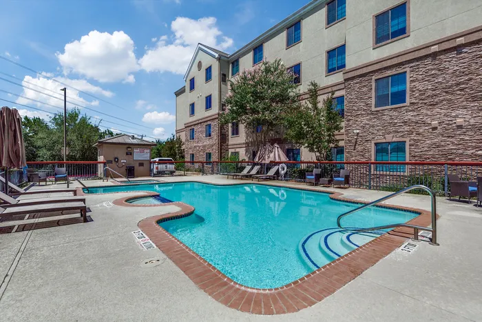 Outdoor pool area with surrounding seating and a view of the building exterior.