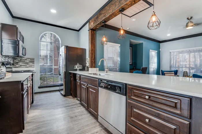 Kitchen area with stainless steel appliances, a large countertop, pendant lighting, and bright windows.
