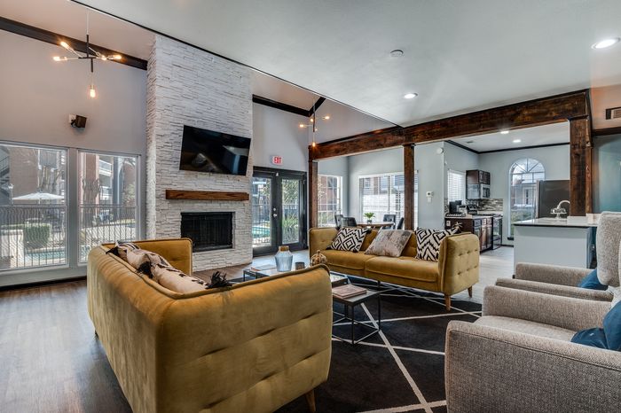 A spacious resident clubhouse featuring seating areas, a fireplace, and a small kitchenette with stainless appliances.