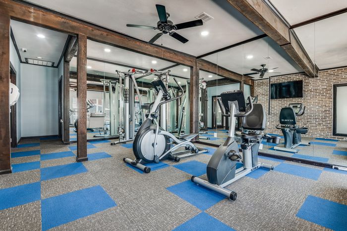 Exercise room featuring cardio machines, strength equipment, mirrored walls, and patterned flooring.