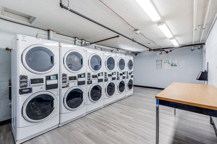 Modern laundry room featuring a row of high-efficiency washers and dryers, complemented by sleek laminate flooring and ample overhead lighting.