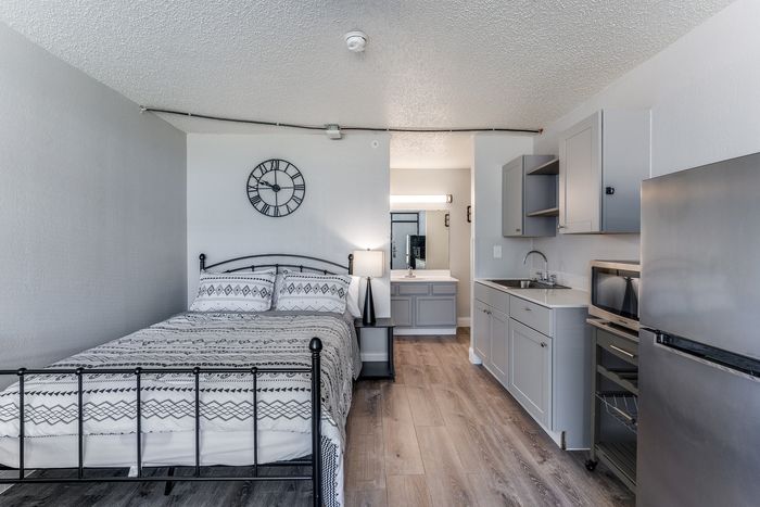 Chic studio apartment with modern decor, featuring a cozy bed, stylish kitchenette, and sleek wooden flooring.