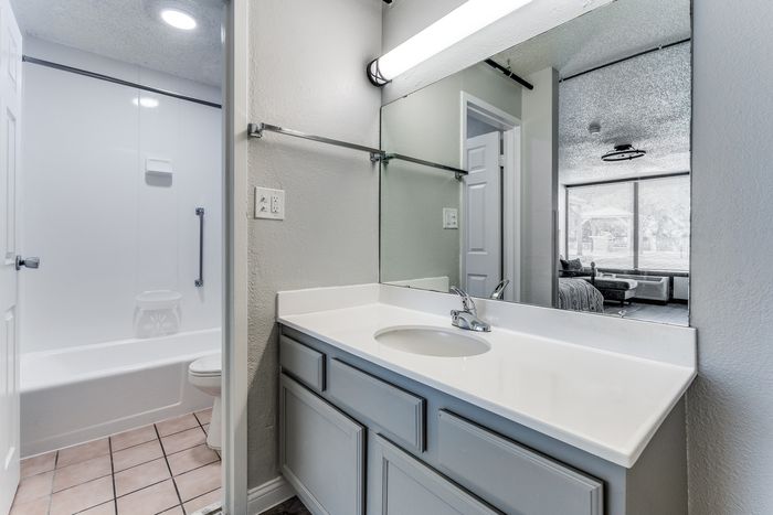 Chic bathroom with modern vanity, sleek mirror, and view of a stylish living area through the doorway.